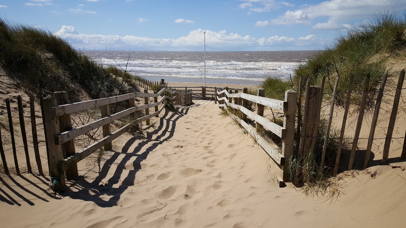 the entrance to sandy beach at formby with grassy dunes and the distant sea on a clear day