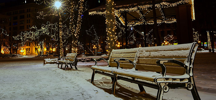 bench covered in snow at winter time with christmas lights in the background