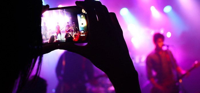 someone holding a mobile phone taking a video of a band performing in a nightclub