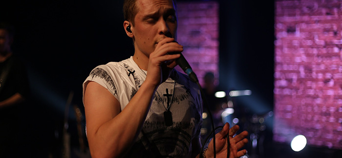 a man singing into a microphone on stage with a band behind him playing drums and guitar